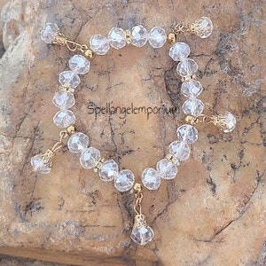 May include: A clear crystal bracelet with gold accents and a dangling crystal charm. The bracelet is made of faceted crystal beads and has a delicate, feminine look.