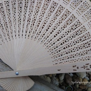 May include: A light brown wooden folding fan with a delicate floral pattern cut out of the wood. The fan is closed and has a metal rivet on the handle.