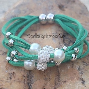 May include: A green leather wrap bracelet with silver beads and a white pearl and rhinestone charm. Spellangelemporium is printed on the bracelet.