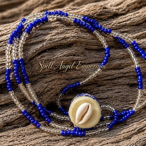 May include: A multi-strand necklace featuring alternating segments of vibrant royal blue and clear glass beads. The necklace includes a central circular pendant made of a light-colored material, inlaid with a single white cowrie shell. The text Spell Angel Emporium is visible.