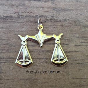 May include: Gold-colored pendant charm in the shape of a scale of justice. The scales are balanced and have a decorative design. The charm is suitable for jewelry making.