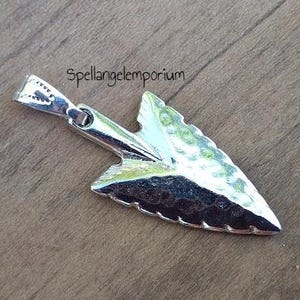 Op de afbeelding: Zilveren pijlpunt hanger met een gehamerde textuur. De hanger heeft een lus aan de bovenkant om aan een ketting of koord te bevestigen.