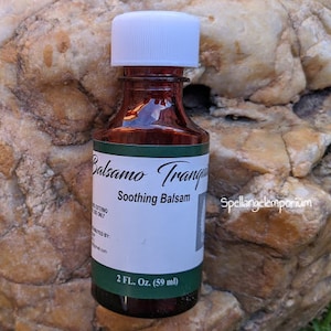 May include: A small brown glass bottle with a white lid. The bottle is labeled "Balsamo Tranquilo" and "Soothing Balsam". The bottle contains 2 fl. oz. (59 ml) of liquid.