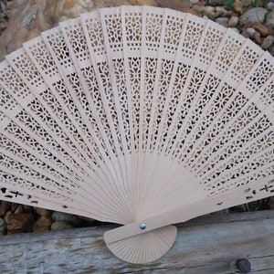 May include: A light beige wooden folding fan with a delicate, intricate cut-out design. The fan is closed and has a wooden handle.