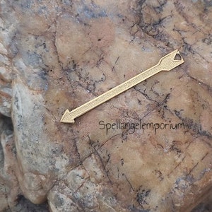 Puede incluir: Un amuleto de flecha de oro con una superficie texturizada. La flecha mide aproximadamente 5 cm de largo.