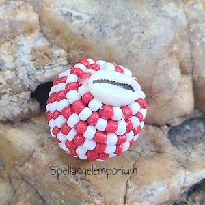 May include: Red and white beaded ball with a white cowrie shell in the center. The ball is about the size of a golf ball.