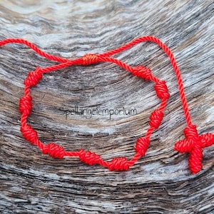 May include: A red knotted bracelet with a red cross charm. The bracelet is made of string and has a simple design.