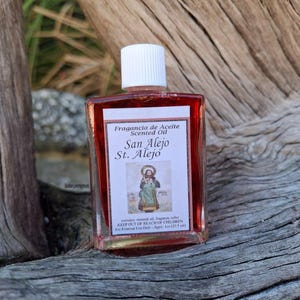 May include: A small glass bottle of red scented oil with a white label. The label reads "Fragancia de Aceite Scented Oil San Alejo St. Alejo". The bottle features a small image of a saint with a halo.