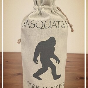 May include: A white canvas bag with a black silhouette of Bigfoot and the text "Sasquatch Fire Water".