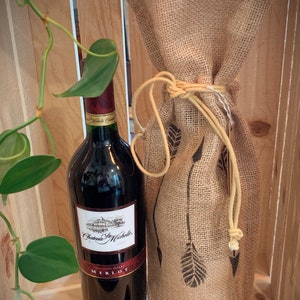 May include: A bottle of Chateau Ste. Michelle Merlot wine in a burlap wine bag with a brown twine tie. The wine bottle is in a wooden crate.