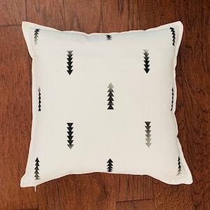 Puede incluir: Almohada blanca con un patrón geométrico negro y gris de flechas. La almohada tiene un fondo blanco y un borde blanco.
