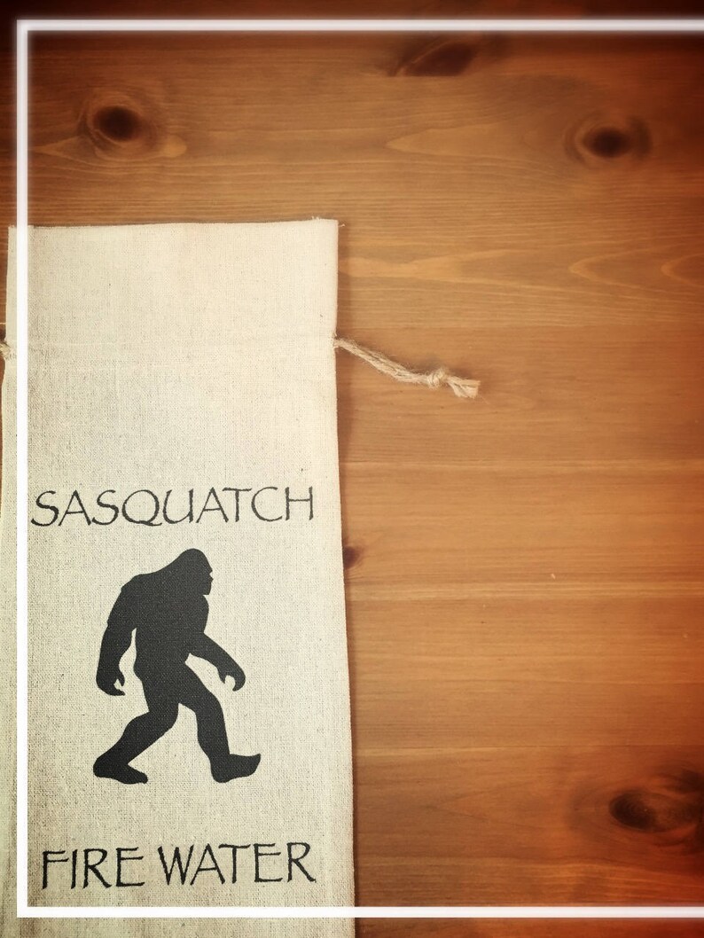 May include: A white canvas bag with the words "Sasquatch Fire Water" printed in black. The bag features a black silhouette of a Sasquatch walking.