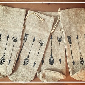 May include: Four brown burlap wine bottle bags with black arrow designs.