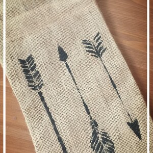 May include: A burlap bag with a drawstring closure features three black arrow designs. The bag is perfect for gift wrapping or storing small items.