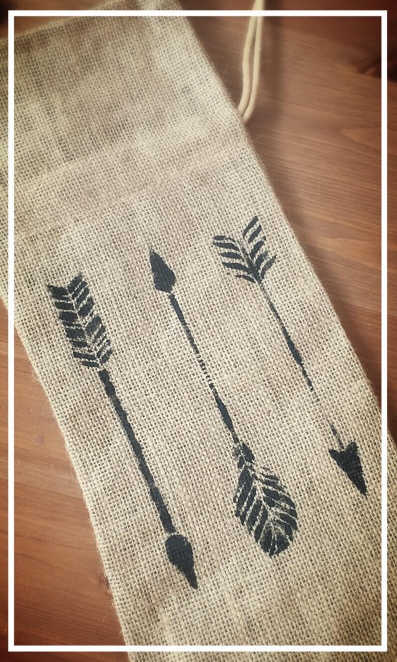 May include: A burlap bag with a drawstring closure features three black arrow designs. The bag is perfect for gift wrapping or storing small items.