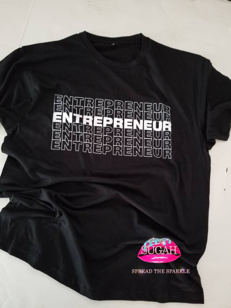 May include: Black t-shirt with the word "ENTREPRENEUR" repeated in white text. The shirt has a pink lip logo with the word "SUGAH" and the text "SPREAD THE SPARKLE" underneath.