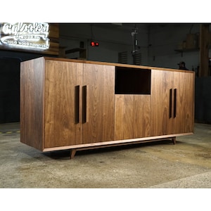 May include: A solid wood entertainment center with six doors and a center open shelf. The cabinet is made of walnut wood and has a dark brown finish. The cabinet has a modern design with angled legs.