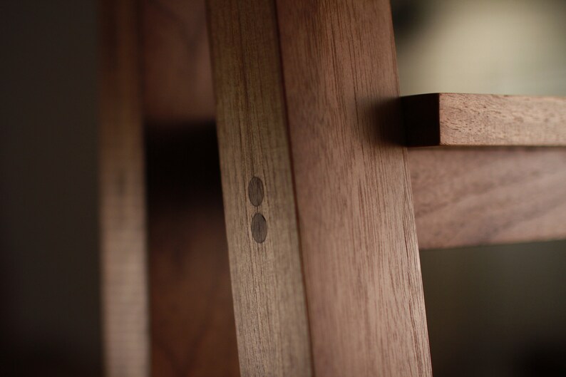 Op de afbeelding: Close-up van een houten plank met twee donkerbruine houten pinnen aan de zijkant van de plank. De plank is gemaakt van massief hout en heeft een natuurlijke afwerking.