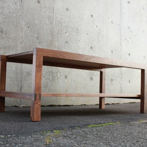 May include: A wooden coffee table with a lower shelf. The table is made of dark brown wood and has a simple, rectangular design.