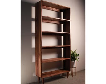 Könnte beinhalten: Ein hohes, hölzernes Bücherregal mit fünf Regalbrettern und einer dunkelbraunen Oberfläche. Das Bücherregal hat ein schlichtes, modernes Design mit spitz zulaufenden Beinen.