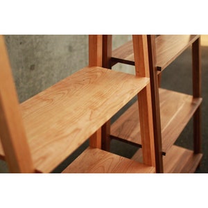 Op de afbeelding: Een houten boekenkast met een lichte houtkleur en een donkerder hout accent. De planken zijn gemaakt van massief hout en hebben een natuurlijke houtnerf.
