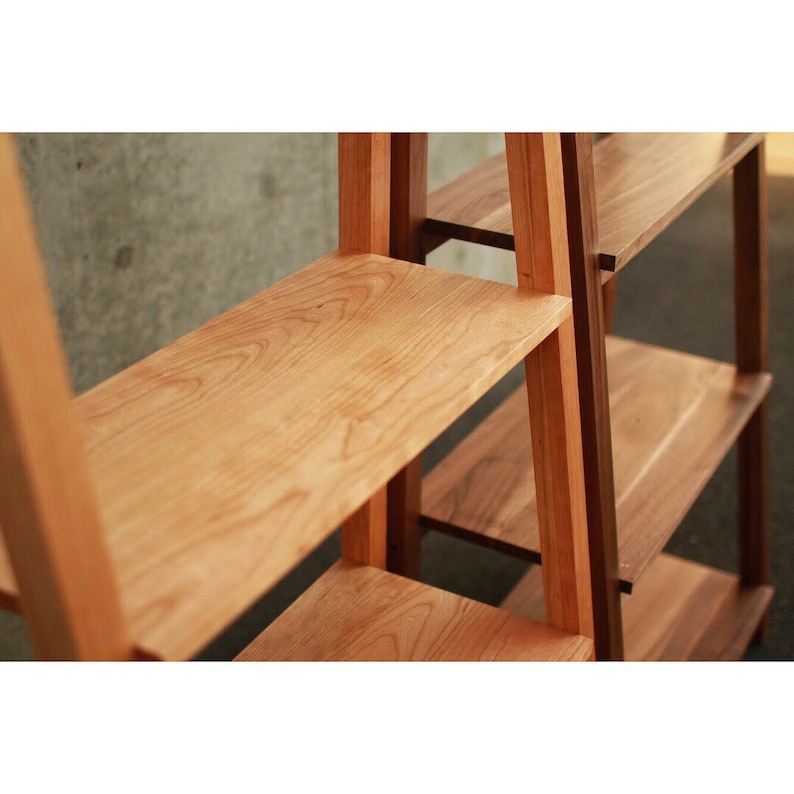 Op de afbeelding: Een houten boekenkast met een lichte houtkleur en een donkerder hout accent. De planken zijn gemaakt van massief hout en hebben een natuurlijke houtnerf.