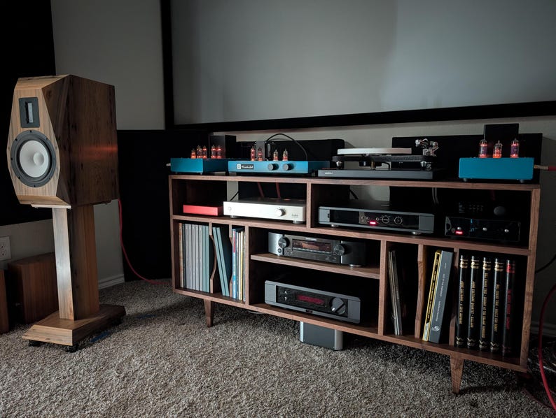 K&ouml;nnte beinhalten: Ein h&ouml;lzernes Audiosystem mit einem gro&szlig;en Lautsprecher auf einem St&auml;nder und einem Schrank im Mid-Century-Modern-Stil. Der Schrank enth&auml;lt verschiedene Audiokomponenten, Schallplatten und B&uuml;cher. Der Lautsprecher ist etwa 102 cm hoch.