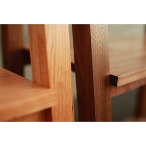 Op de afbeelding: Close-up van twee houten planken, een van licht hout en de andere van donker hout. De planken zijn met een rechte hoek aan elkaar bevestigd, waardoor een hoekplank-eenheid ontstaat.