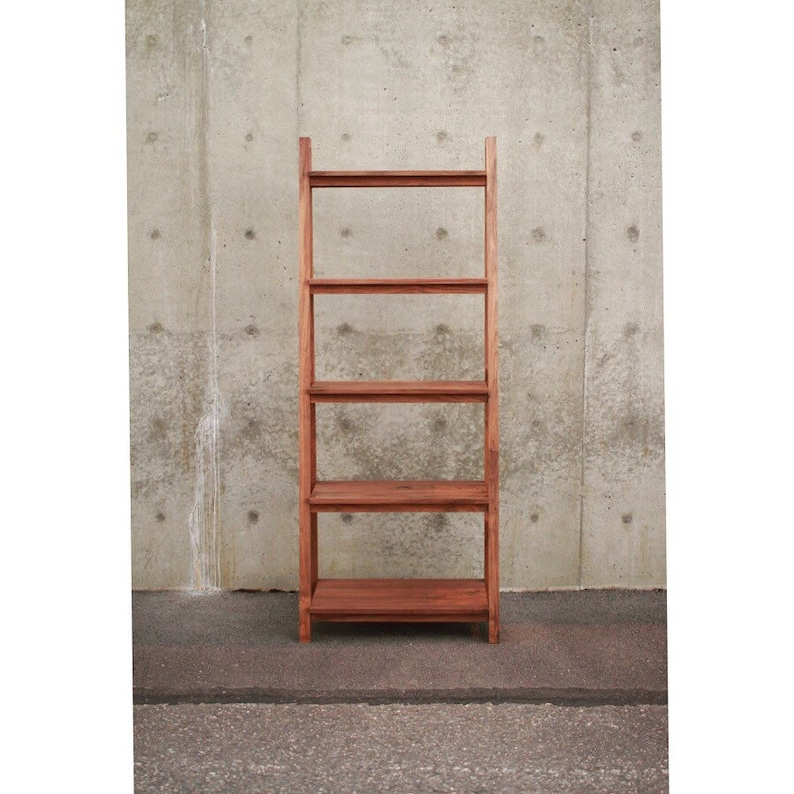 Op de afbeelding: Een houten ladderrek met vijf planken. Het rek is gemaakt van donkerbruin hout en staat voor een betonnen muur.