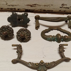 Può includere: Assortimento di tiretti e pomelli per cassetti in ottone antico. I tiretti presentano disegni decorativi con una finitura usurata. I pomelli sono rotondi con un centro rialzato e dettagli intricati.