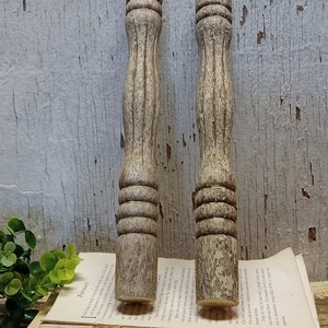 May include: Two wooden turned spindles with a distressed white paint finish. The spindles have a fluted design and are approximately 10 inches long.