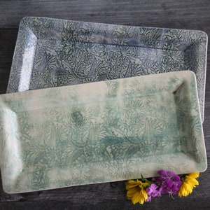 May include: Two rectangular ceramic serving trays with a raised floral design. The top tray is blue and white, and the bottom tray is green and white.