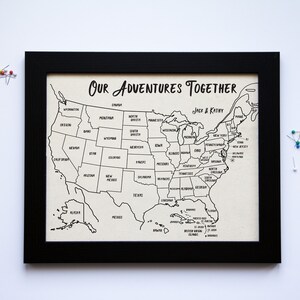 May include: A black framed map of the United States with the text "Our Adventures Together" and "Jack & Katy" printed on it. The map is designed for marking locations with push pins.