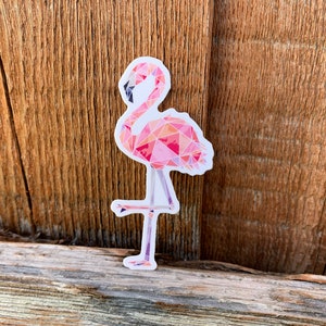 Puede incluir: Una pegatina de flamenco rosa con un dise&ntilde;o geom&eacute;trico. El flamenco est&aacute; de pie sobre una sola pierna y tiene un cuello largo.