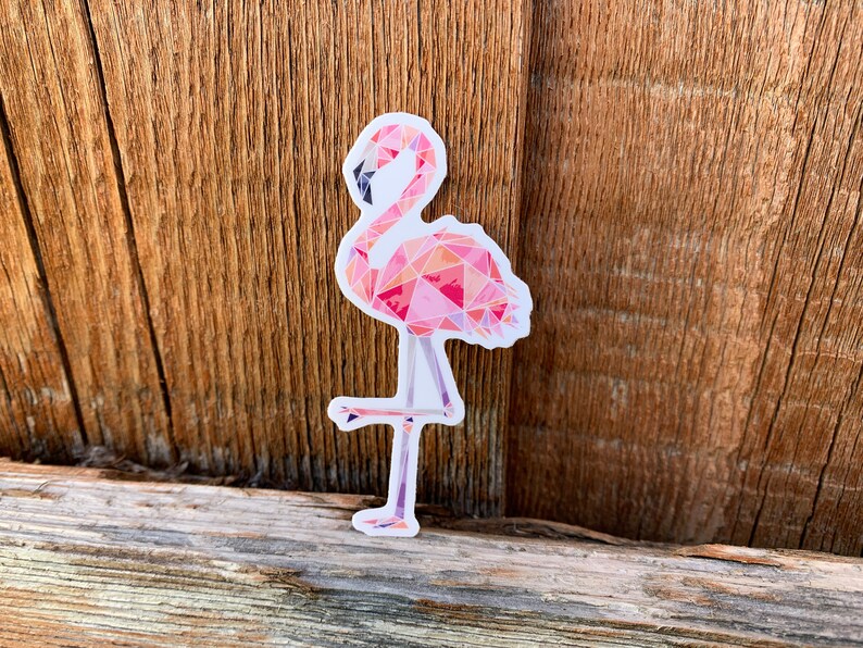 Puede incluir: Una pegatina de flamenco rosa con un dise&ntilde;o geom&eacute;trico. El flamenco est&aacute; de pie sobre una sola pierna y tiene un cuello largo.