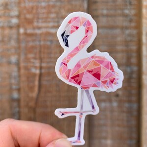 Puede incluir: Una pegatina de flamenco rosa con un dise&ntilde;o geom&eacute;trico. El flamenco est&aacute; de pie sobre una sola pierna y tiene un cuello largo.