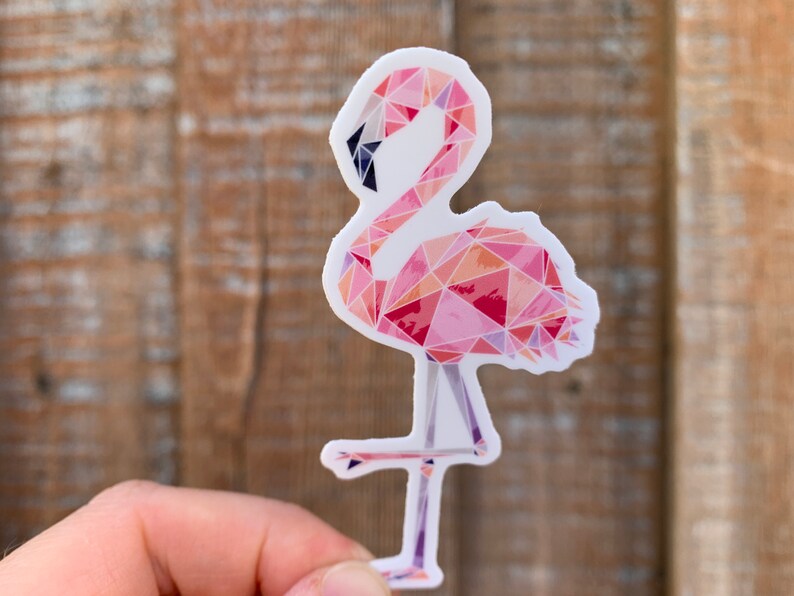 Puede incluir: Una pegatina de flamenco rosa con un dise&ntilde;o geom&eacute;trico. El flamenco est&aacute; de pie sobre una sola pierna y tiene un cuello largo.
