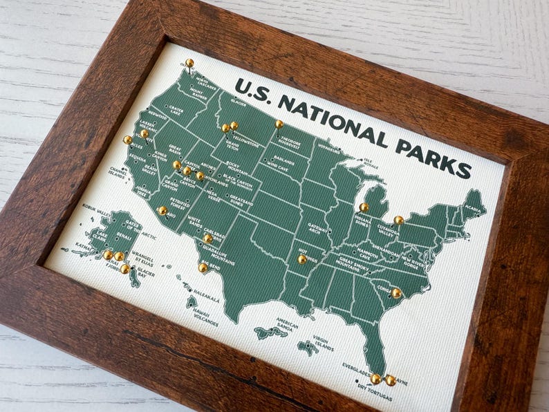 Pu&ograve; includere: Una mappa incorniciata dei parchi nazionali degli Stati Uniti. La mappa &egrave; verde con testo bianco e puntine dorate che segnano le posizioni dei parchi. La cornice &egrave; in legno marrone scuro. Le parole "U.S. NATIONAL PARKS" sono stampate in alto.