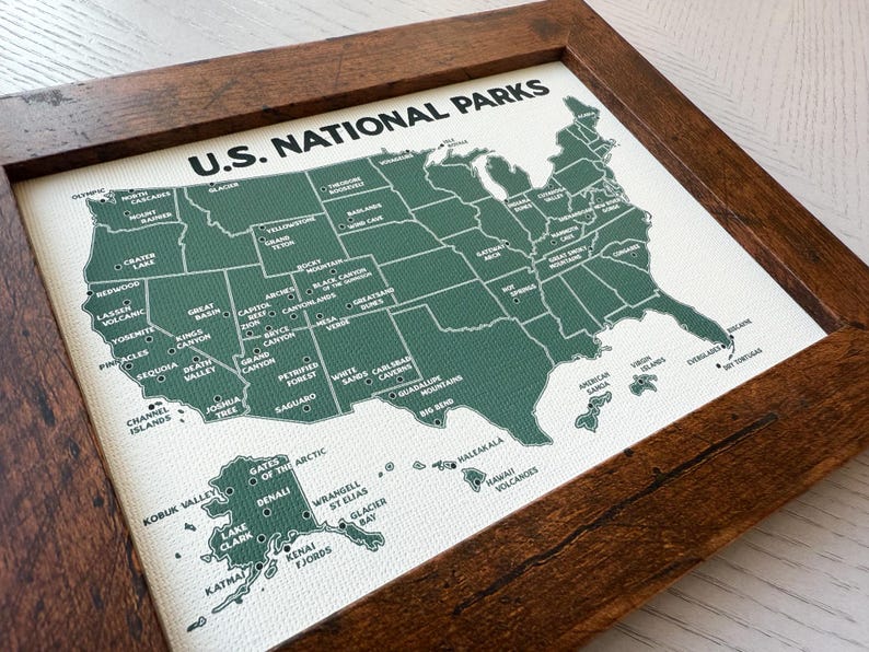 Pu&ograve; includere: Una mappa incorniciata dei parchi nazionali degli Stati Uniti. La mappa &egrave; verde su sfondo bianco, con ogni parco etichettato. La cornice &egrave; in legno marrone scuro. Le parole "U.S. NATIONAL PARKS" sono stampate in alto.