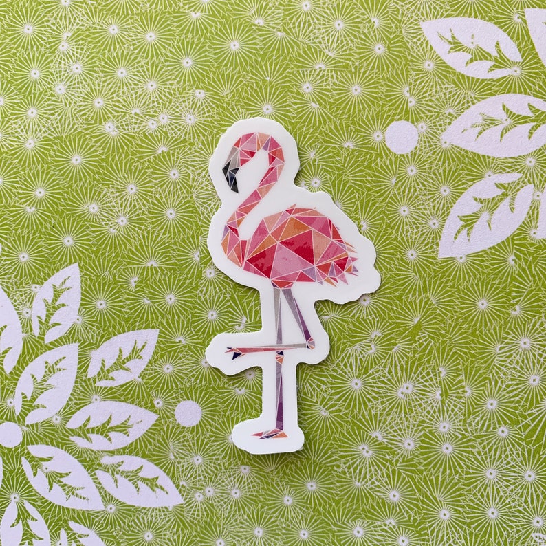 Puede incluir: Una pegatina de flamenco rosa con un dise&ntilde;o geom&eacute;trico. El flamenco est&aacute; de pie sobre una pierna con la cabeza inclinada hacia abajo. La pegatina est&aacute; sobre un fondo verde con un patr&oacute;n floral blanco.