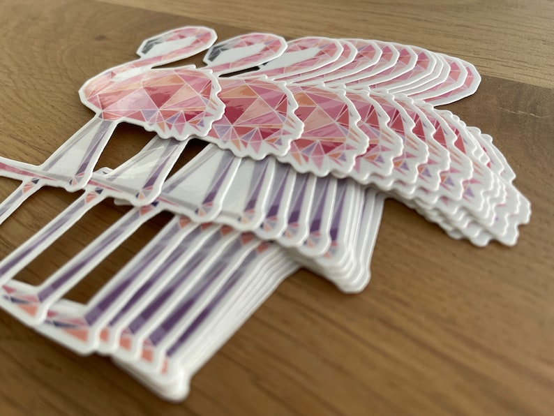 Puede incluir: Una pila de pegatinas de flamencos rosas con un dise&ntilde;o geom&eacute;trico. Las pegatinas est&aacute;n hechas de un material brillante y tienen un fondo blanco.