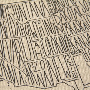 May include: A close-up of a beige fabric with a black outline of the United States of America. Each state is labeled with its name.