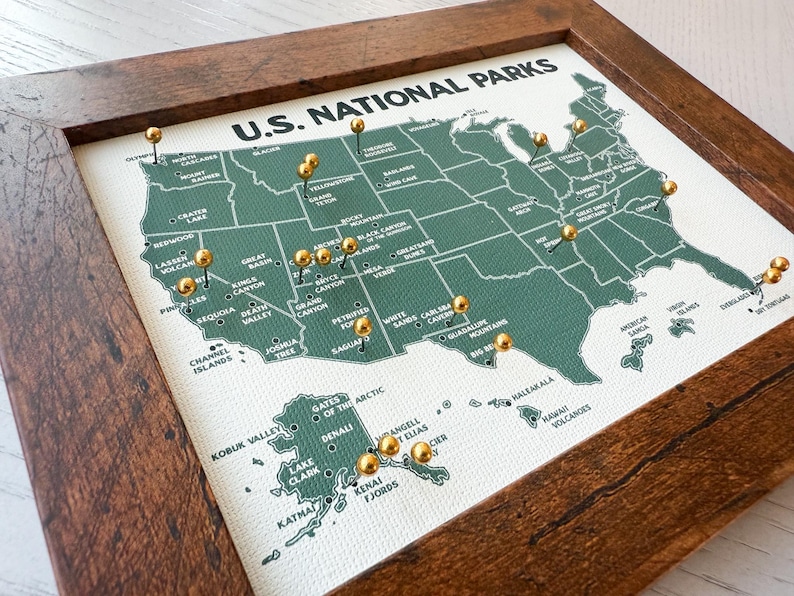 Pu&ograve; includere: Una mappa incorniciata dei parchi nazionali degli Stati Uniti con un contorno verde degli Stati Uniti. Spilli dorati segnano varie localit&agrave; dei parchi. La mappa &egrave; etichettata "U.S. NATIONAL PARKS" in testo bianco ed &egrave; incorniciata in una cornice di legno marrone scuro.