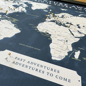 May include: A world map with gold push pins marking locations. The map is on a dark blue background with the text "Adventure Awaits" and "Past Adventures to Come" printed on the bottom.