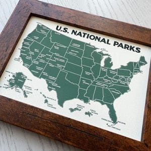Pu&ograve; includere: Una mappa incorniciata degli Stati Uniti, che evidenzia i parchi nazionali in verde su uno sfondo bianco. La mappa &egrave; etichettata "U.S. NATIONAL PARKS" in testo nero ed &egrave; racchiusa in una cornice di legno marrone scuro.