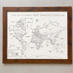 May include: A framed world map print on a white background with black outlines of continents and countries. The text "LIFE IS A JOURNEY BEST TRAVELED TOGETHER" is printed in black at the top. The frame is made of dark brown wood with a textured finish.