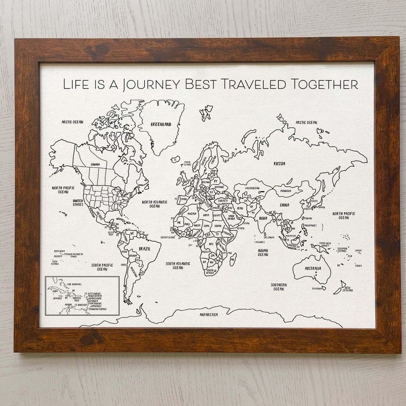May include: A framed world map print on a white background with black outlines of continents and countries. The text "LIFE IS A JOURNEY BEST TRAVELED TOGETHER" is printed in black at the top. The frame is made of dark brown wood with a textured finish.