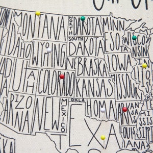 May include: A map of the United States with push pins in various colors marking different states. The map is printed on a white canvas background. The states are outlined in black and the names of the states are written in black.