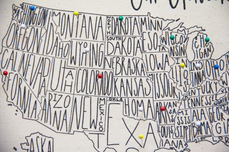 May include: A map of the United States with push pins in various colors marking different states. The map is printed on a white canvas background. The states are outlined in black and the names of the states are written in black.