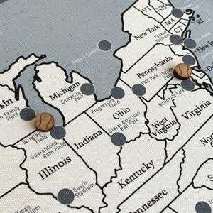 May include: A map of the United States with wooden baseball pins marking different locations. The pins are placed on the map in the locations of various baseball stadiums.